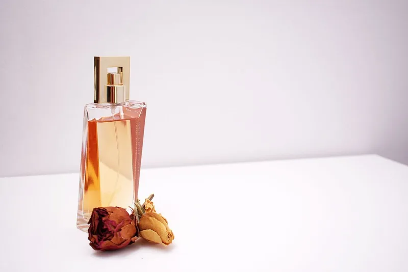 Amber perfume bottle on a pale pink set with two dried roses beside it