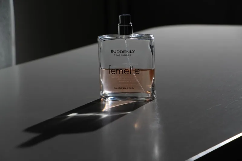 Clear glass perfume bottle on a dark table with a long cast shadow